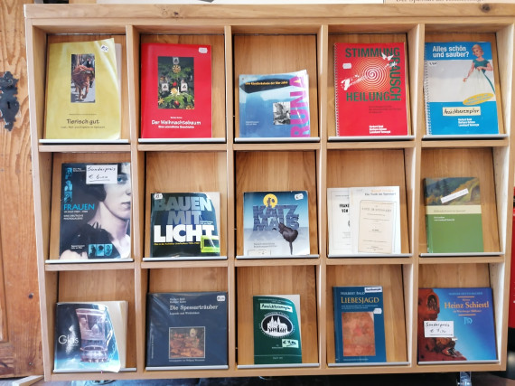 Hölzernes Bücherregal im Museumsladen, das mit 15 Fächern ausgestattet ist. Vor jedem Fach steht ein Ansichtsexemplar der Eigenpublikationen des Spessartmuseums